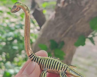 May include: A bronze-colored, stylized figurine of a plesiosaur, a prehistoric marine reptile. The figurine has a long neck, small head, and flipper-like appendages. The body is detailed with ribbed markings.