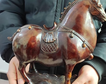 Puede incluir: Escultura detallada de un caballo marrón con silla de montar. La escultura tiene un acabado brillante y la sostiene una persona. El caballo está sobre una base que parece agua. Es un objeto decorativo.