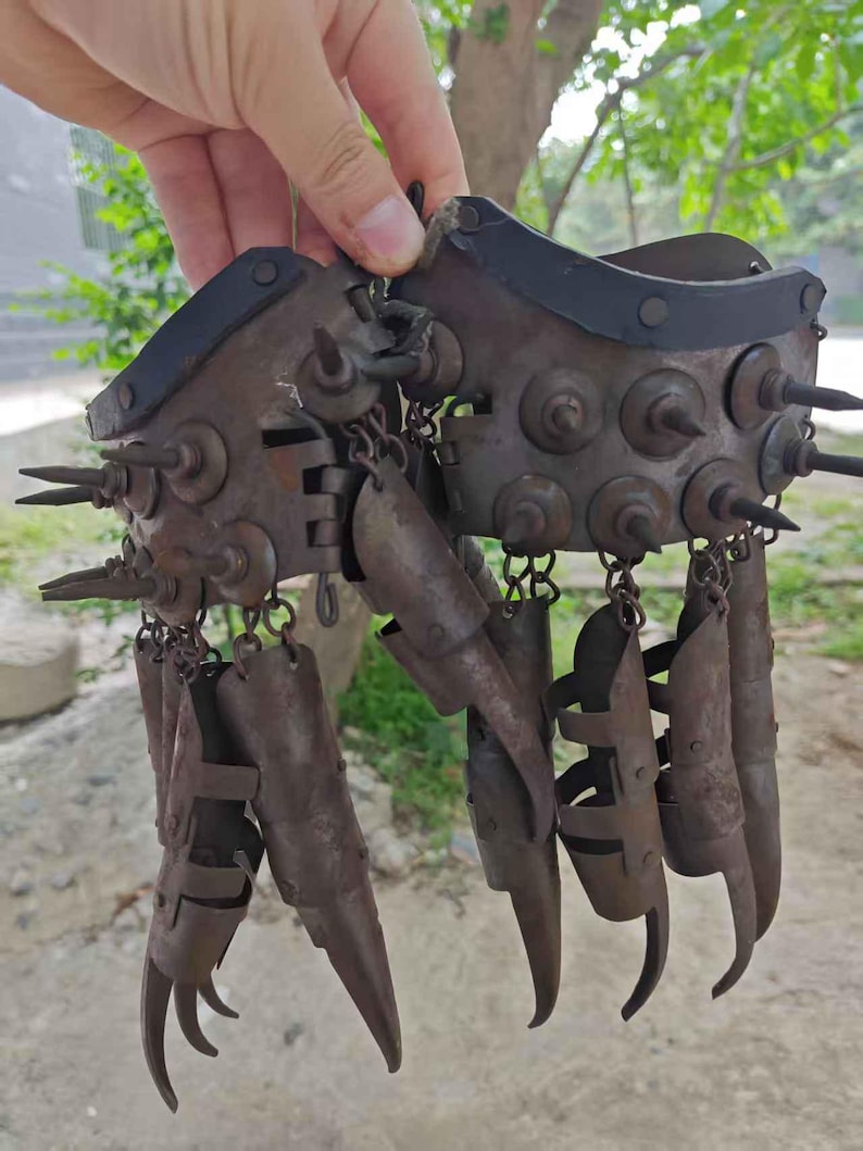 Pu&ograve; includere: Un paio di artigli per dita antichi in metallo, tenuti in mano. Gli artigli sono in metallo arrugginito, con punte affilate e ricurve. Il design include un braccialetto a punte e coperture individuali per le dita, collegate da catene.