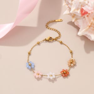Puede incluir: Una pulsera dorada con una delicada cadena y coloridos abalorios de flores con cuentas. La pulsera tiene un cierre de mosquet&oacute;n y est&aacute; adornada con detalles florales azules, rosas, blancos y naranjas. Una joya encantadora.
