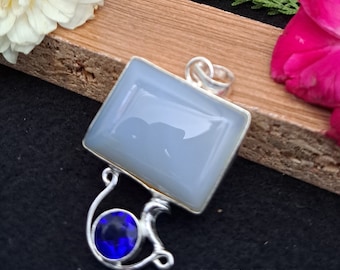May include: A silver pendant with a large, light blue, rectangular stone and a smaller, round, dark blue stone. The pendant has a unique, curved design and is set against a dark background with flowers and the text "DSCRFTART".