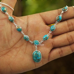 Könnte beinhalten: Eine silberne Halskette mit ovalen türkisfarbenen und kupferfarbenen Steinen. Die Halskette hat eine filigrane Kette und einen Anhänger mit einem größeren Türkisstein. Die Halskette wird auf einer Hand präsentiert.
