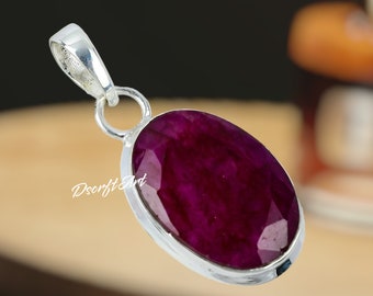 Può includere: Ciondolo in argento con una grande gemma di rubino ovale e sfaccettata. Il rubino è di un colore rosso intenso e ricco. Il ciondolo ha un design semplice con un anello per una catena. Il nome del marchio "Dscrft Art" è stampato.