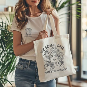Puede incluir: Bolsa de tela blanca con una ilustraci&oacute;n en blanco y negro de una mujer con serpientes como cabello. El texto "The Female Gaze" y "Petrify the Patriarchy" est&aacute; impreso en la bolsa.