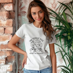 Puede incluir: Camiseta blanca con un gr&aacute;fico en blanco y negro de Medusa con serpientes en el pelo. El texto "The Female Gaze" y "Petrify the Patriarchy" est&aacute; impreso en la camiseta.