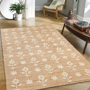 May include: A beige area rug with a white floral pattern. The rug is made of natural fibers and has a woven texture.