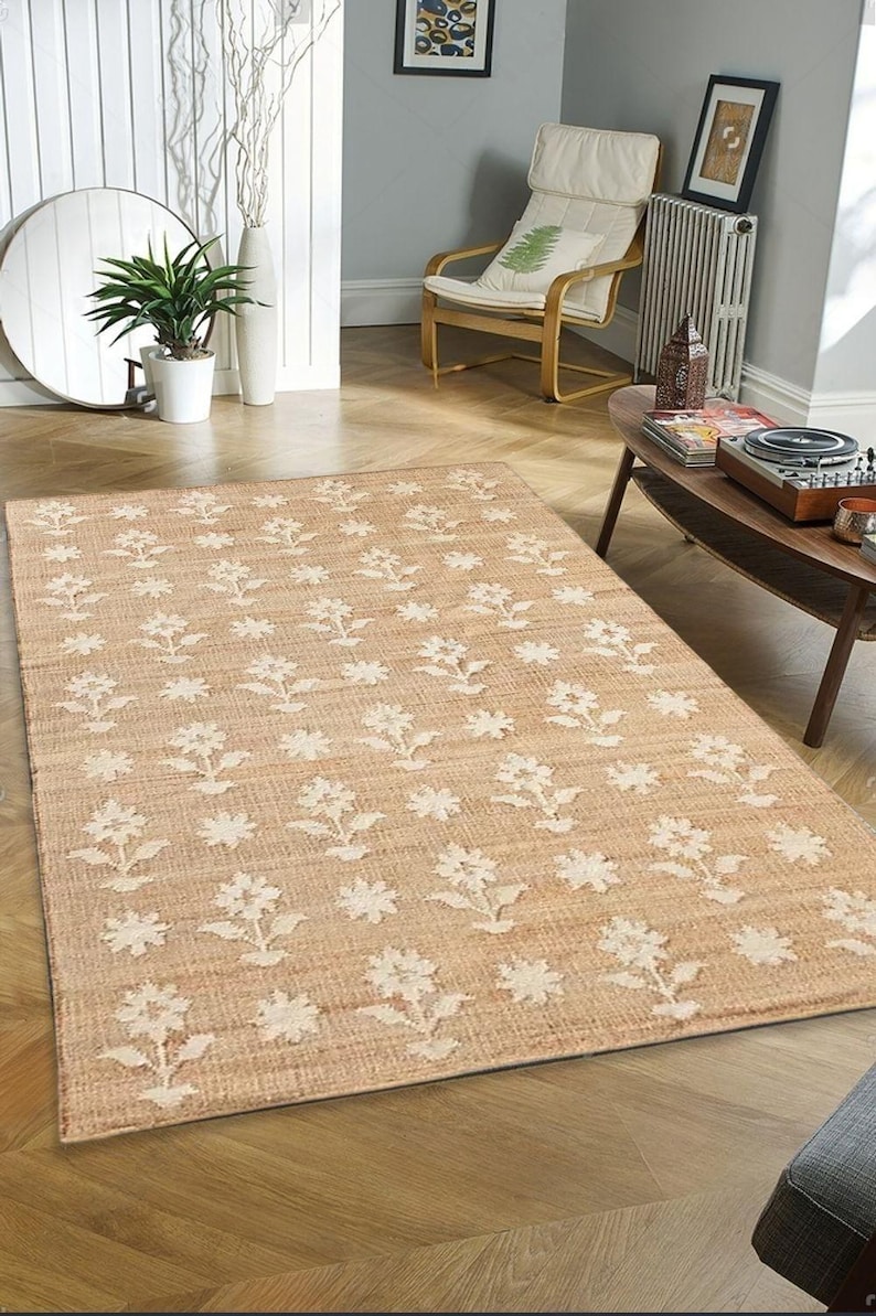 May include: A beige area rug with a white floral pattern. The rug is made of natural fibers and has a woven texture.