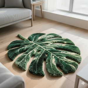 Puede incluir: Una alfombra verde y blanca con forma de hoja. La alfombra está diseñada para parecerse a una hoja de planta de Monstera, con vetas detalladas y secciones recortadas. La alfombra está hecha de un material suave y texturizado.
