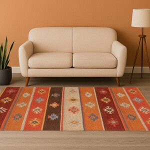 May include: A rectangular area rug with a striped pattern in shades of orange, red, brown, and cream. The rug features geometric designs within each stripe. A beige sofa and a floor lamp are in the background.