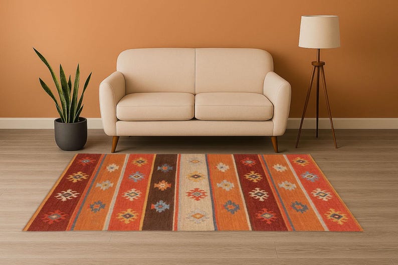 May include: A rectangular area rug with a striped pattern in shades of orange, red, brown, and cream. The rug features geometric designs within each stripe. A beige sofa and a floor lamp are in the background.