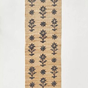 May include: A natural fiber rug with a floral pattern in black. The rug is woven with a subtle texture and has a rectangular shape.