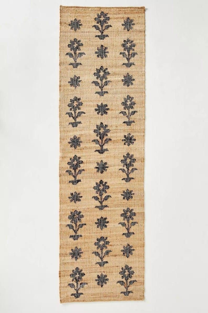 May include: A natural fiber rug with a floral pattern in black. The rug is woven with a subtle texture and has a rectangular shape.