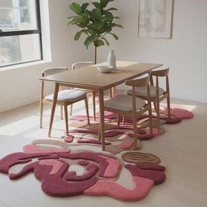 Peut inclure: Une salle &agrave; manger avec une table et des chaises en bois, et un grand tapis abstrait dans les tons de rose, beige et marron. Une plante verte et une &oelig;uvre d'art sont &eacute;galement visibles.