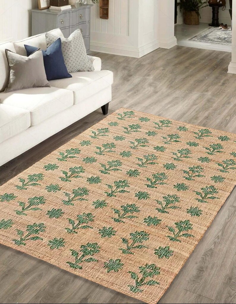 May include: A beige and green floral patterned rug with a woven texture. The rug is laid out on a hardwood floor in a living room setting.