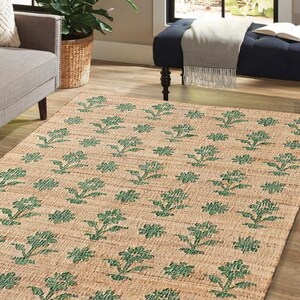 May include: A natural fiber rug with a floral pattern. The rug is woven with a beige background and green floral designs.