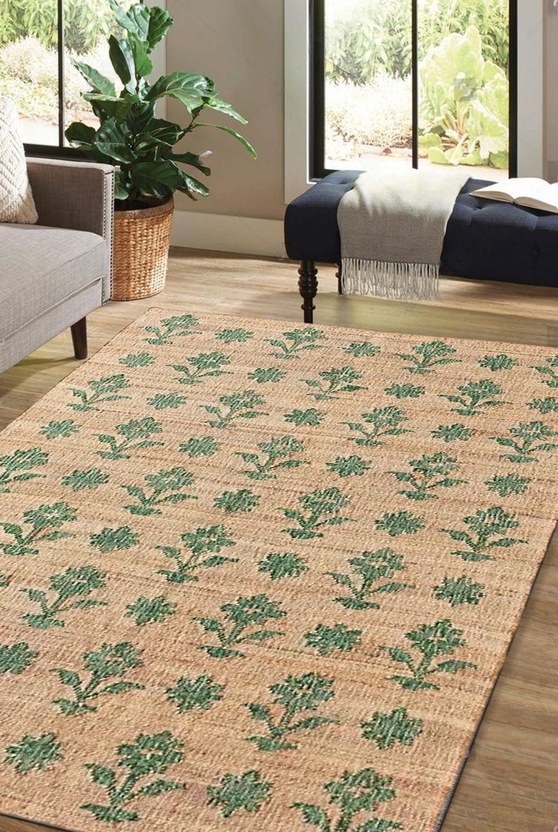 May include: A natural fiber rug with a floral pattern. The rug is woven with a beige background and green floral designs.