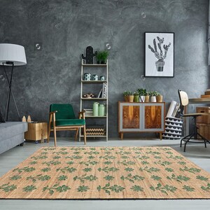 May include: A green and brown patterned rug with a floral design. The rug is laid out in a living room with a gray sofa, a green armchair, and a wooden cabinet.