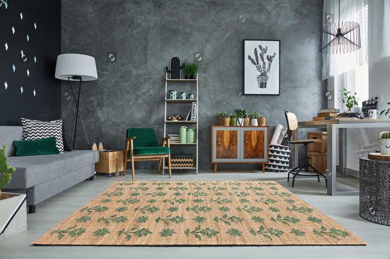 May include: A green and brown patterned rug with a floral design. The rug is laid out in a living room with a gray sofa, a green armchair, and a wooden cabinet.