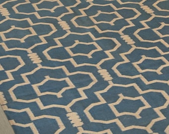 May include: A blue and beige geometric patterned rug. The rug features a repeating pattern of interlocking shapes in a light beige color against a deep blue background. The rug is rectangular and appears to be made of a woven material.