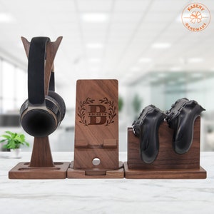 May include: A wooden stand with three compartments for organizing gaming accessories. The stand has a headphone holder, a phone stand with a personalized inscription "BOBBY", and a controller holder.