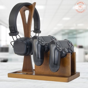 May include: A wooden gaming station with a headset and two black controllers. The headset is black with a leather-like texture. The station is made of dark brown wood and has a small tray at the base.