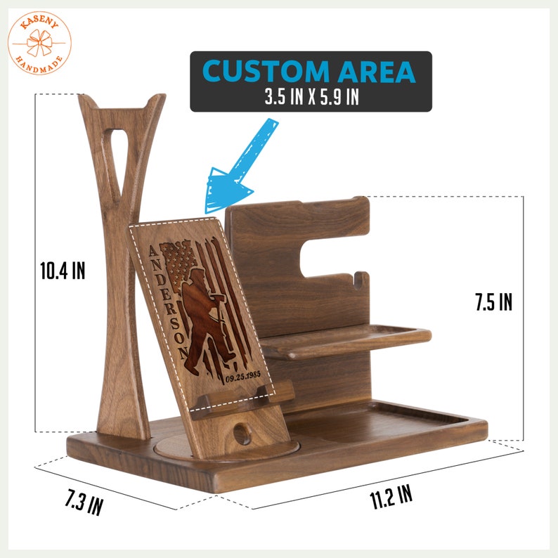 May include: A wooden phone stand with a custom engraved design featuring a person holding an American flag and the text "ANDERSON 09.25.1985". The stand has a phone holder, a watch holder, and a tray for other items. The stand is 11.2 inches wide, 7.5 inches tall, and 7.3 inches deep. The custom area is 3.5 inches by 5.9 inches.