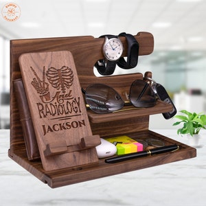 May include: A wooden desktop organizer with a phone stand, watch holder, and slots for keys, glasses, and other items. The organizer is personalized with the text "Peace and Radiology Jackson".