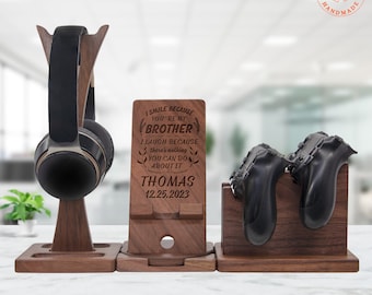 May include: A wooden desk organizer set with a headphone stand, phone holder, and controller stand. The phone holder is engraved with the text "I SMILE BECAUSE YOU'RE MY BROTHER" and a name and date. The headphone stand holds a black and silver headset.