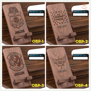 May include: Four wooden phone stands with different designs. Each stand features a laser-engraved emblem, a name, and the text "CUSTOM TEXT LINE I". The emblems include a CBP Border Patrol badge, a U.S. Border Patrol badge, a U.S. Customs and Border Protection badge, and a BORTAC badge.