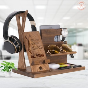 May include: A wooden desktop organizer with a phone stand, watch holder, glasses holder, and headphone hook. It has an engraved message that reads "Life is better when you're aligned" and "Dr. David".