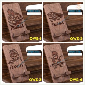 May include: Wooden phone stands with engraved welder designs. Each stand features a different welder graphic and a name, such as "THOMAS" or "DAVID". The stands are made of dark wood and have a slot to hold a phone.