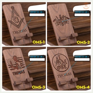 May include: Four wooden phone stands with different engraved designs. Each stand has a slot for holding a phone and a space for a personalized name. The designs include a Masonic symbol, a set of tools, a person holding a flag, and a Masonic symbol with the words "I am one".