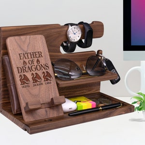May include: A wooden organizer with a phone stand, watch holder, and compartments for keys, glasses, and other items. The organizer has an engraved message that reads "Father of Dragons" with the names Olivia, Jackson, and Emma below.