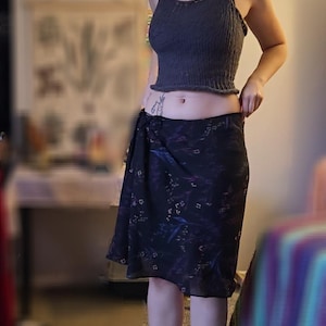 May include: A dark gray halter top and a black skirt with a floral pattern. The skirt is knee-length. The person is wearing black socks with a green alien design.