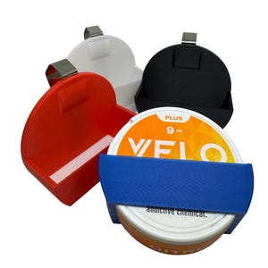 May include: A collection of colorful, 3D-printed containers, each with a hinged lid and a metal clip. One container is red, another white, and a third is black. A blue band holds a circular container with the text "VELO" and "CITRUS".