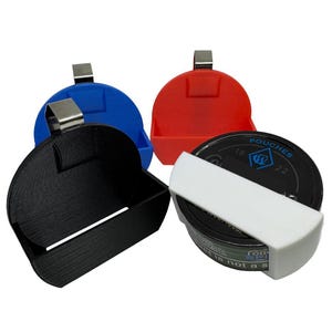 May include: A collection of four plastic containers in black, blue, and red, each with a silver clip. One container holds a black and white item with text. The containers are designed to hold small items.