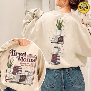 May include: Beige sweatshirt with a graphic on the front and back. The front graphic reads "Tired Moms Book Club" with illustrations of books, coffee, and candles. The back graphic features a stack of books, a coffee cup, and a potted plant.