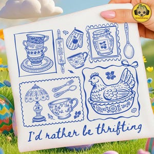 Puede incluir: Bolso tote blanco con ilustraciones en línea azul de artículos de cocina y fiesta de té, incluyendo tazas de té, un rodillo, un tarro de mermelada y una gallina. El texto "I'd rather be thrifting" está impreso en azul en la parte inferior.