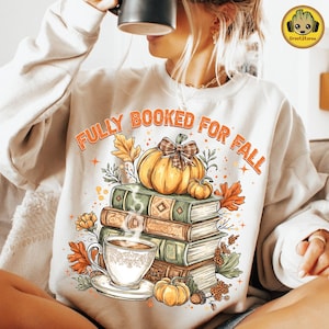Könnte beinhalten: Cremefarbenes Sweatshirt mit dem orangefarbenen Schriftzug "FULLY BOOKED FOR FALL". Die Grafik zeigt einen Bücherstapel, einen Kürbis mit karierter Schleife, eine Tasse Kaffee und Herbstlaub.