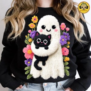 Peut inclure: Sweat-shirt noir avec un fantôme blanc tenant un chat noir, entouré de fleurs brodées colorées. Le fantôme et le chat ont des visages de style dessin animé. Un design amusant pour les amoureux des chats et Halloween.