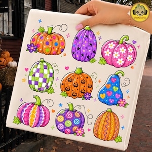 Pode incluir: Uma sacola de tecido branco com uma estampa gráfica colorida de nove abóboras em vários padrões e cores, incluindo laranja, roxo, rosa, verde e azul, decoradas com estrelas, corações, flores e bolinhas.