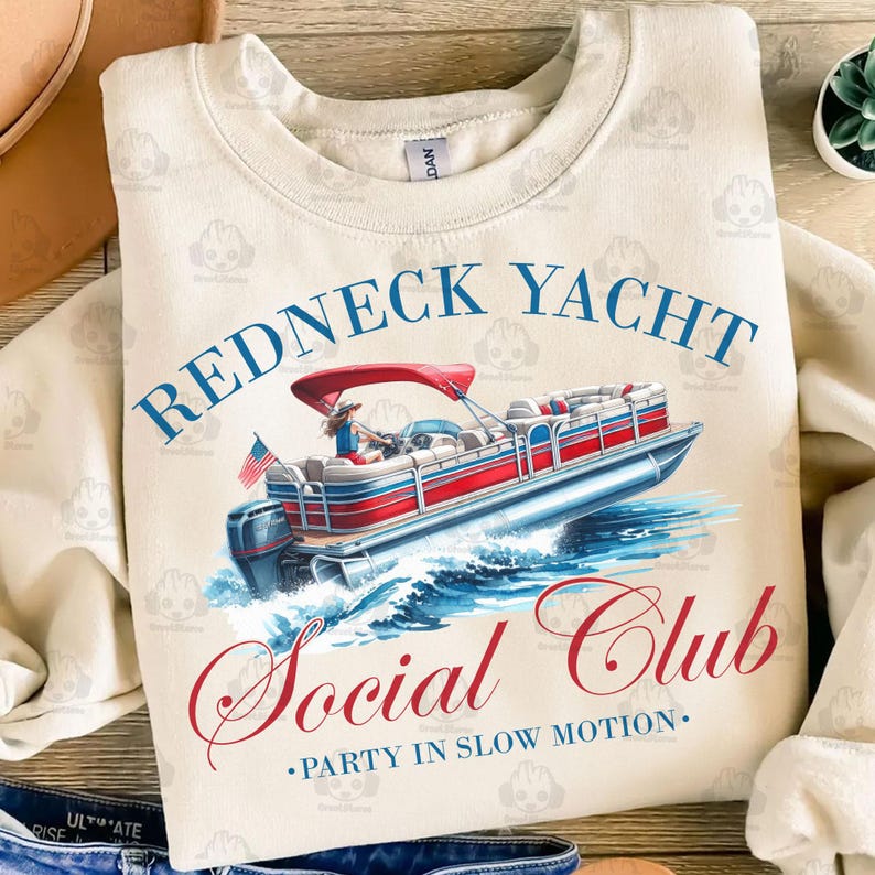 May include: A beige sweatshirt with a red, white, and blue illustration of a pontoon boat on water. The text "Redneck Yacht Social Club - Party in Slow Motion" is printed on the sweatshirt.