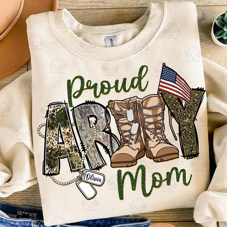 May include: A beige sweatshirt with the words "Proud Army Mom" in green and camouflage print. The word "Army" is made up of camouflage boots and a small American flag. There is a dog tag with the name "Olivia" on it.