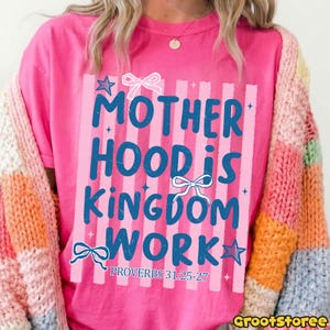 Pu&ograve; includere: Una maglietta rosa acceso con la scritta blu "MOTHERHOOD IS KINGDOM WORK", impreziosita da fiocchi e stelle. Il testo &egrave; posto su strisce verticali rosa. La maglietta include anche il versetto biblico Proverbi 31:25-27.