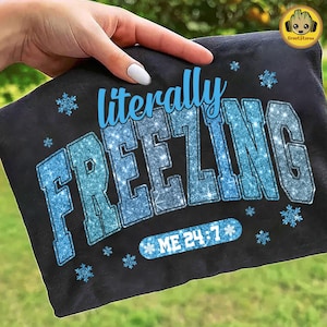 May include: Black t-shirt with the words "literally FREEZING" in a blue, glittery font. The phrase "ME 24-7" is below the main text, also in blue. Small snowflake graphics are scattered around the text.