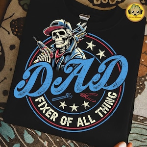 May include: Black t-shirt with a graphic of a skeleton in a cap, holding tools. The design includes the word "DAD" in blue, and the text "FIXER OF ALL THING" in a circular design, with stars and tools.