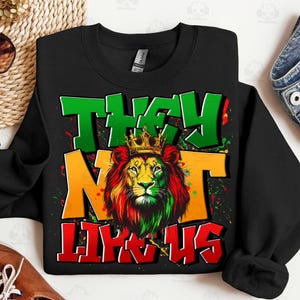 May include: Black sweatshirt with a lion graphic wearing a gold crown. The lion's mane is red, yellow, and green. The words "THEY" and "US" are in green and red, respectively, with "NOT" in yellow.