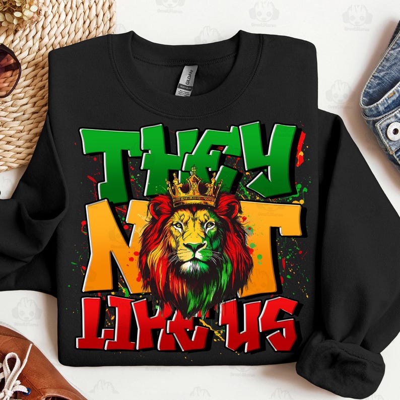 May include: Black sweatshirt with a lion graphic wearing a gold crown. The lion's mane is red, yellow, and green. The words "THEY" and "US" are in green and red, respectively, with "NOT" in yellow.