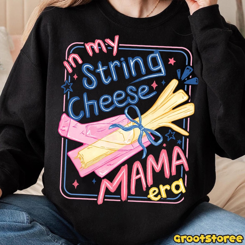 May include: Black sweatshirt with a colorful graphic that reads "In my String Cheese Mama Era." The design features a bundle of string cheese tied with a blue bow, and a pink wrapper. The text is in pink, blue, and yellow.