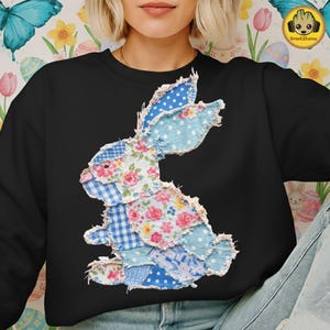 May include: Black sweatshirt featuring a patchwork bunny design. The bunny is composed of various blue and floral patterned fabrics, including polka dots, gingham, and rose prints. The design has a frayed edge, giving it a rustic, handmade appearance. The sweatshirt is a casual, comfortable garment.